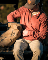 Hidden Lakes 1/4 Zip Knit Pullover model garrett rucker on the talkgate of a side by side in cooler at a campfire in Banded Casual Wear and Lifestyle Apparel. Banded Roll-top cylinder cooler.